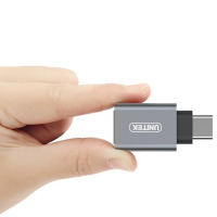 Szary adapter USB Typ-C na USB marki UNITEK trzymany w palcach, ukazujący kompaktową konstrukcję złącza przeznaczoną do laptopów Apple MacBook.