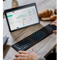 Czarna składana klawiatura Bluetooth Zagg Tri-fold używana przy tablecie z wykresami analitycznymi na ekranie, ustawiona na drewnianym stole obok rogalików.