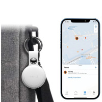 Biały lokalizator MiTag marki MiLí przypięty do szarej torby oraz smartfon z aplikacją Apple Find My pokazującą lokalizację przedmiotu w pobliżu lotniska.
