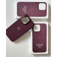 Rubinowe etui Apple FineWoven z MagSafe do iPhone 15 Pro Max leży obok dwóch białych opakowań z nadrukiem nazwy produktu i logo Apple na jasnym tle.