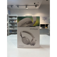 Białe słuchawki bezprzewodowe Bose QuietComfort Ultra w opakowaniu z nadrukiem modelu i napisem Noise Cancelling, widok na pudełko ustawione na blacie.