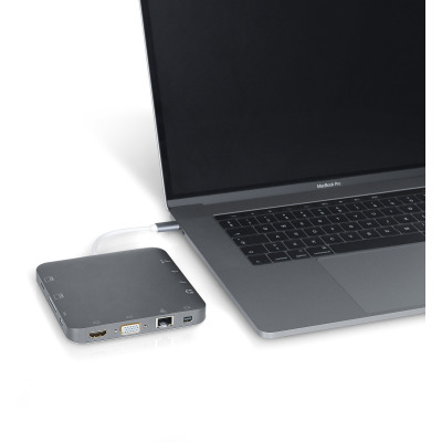 Szara stacja dokująca eSTUFF USB-C Docking Hub podłączona kablem do laptopa Apple MacBook Pro, ukazująca liczne porty wejściowe na bocznej krawędzi urządzenia.