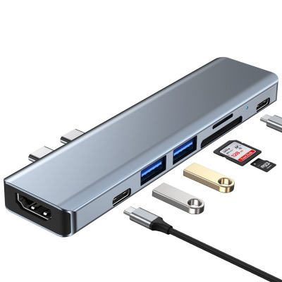 Szary adapter Tech-Protect V5-Hub 7in1 z wieloma portami obok opakowania z grafiką przedstawiającą podłączenie urządzenia do laptopa Apple MacBook.