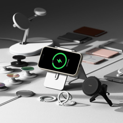 Kremowe etui Ringke Silicone MagSafe na iPhone 16 zamontowane na podstawce ładującej, otoczone akcesoriami magnetycznymi i ładowarkami na jasnym blacie.